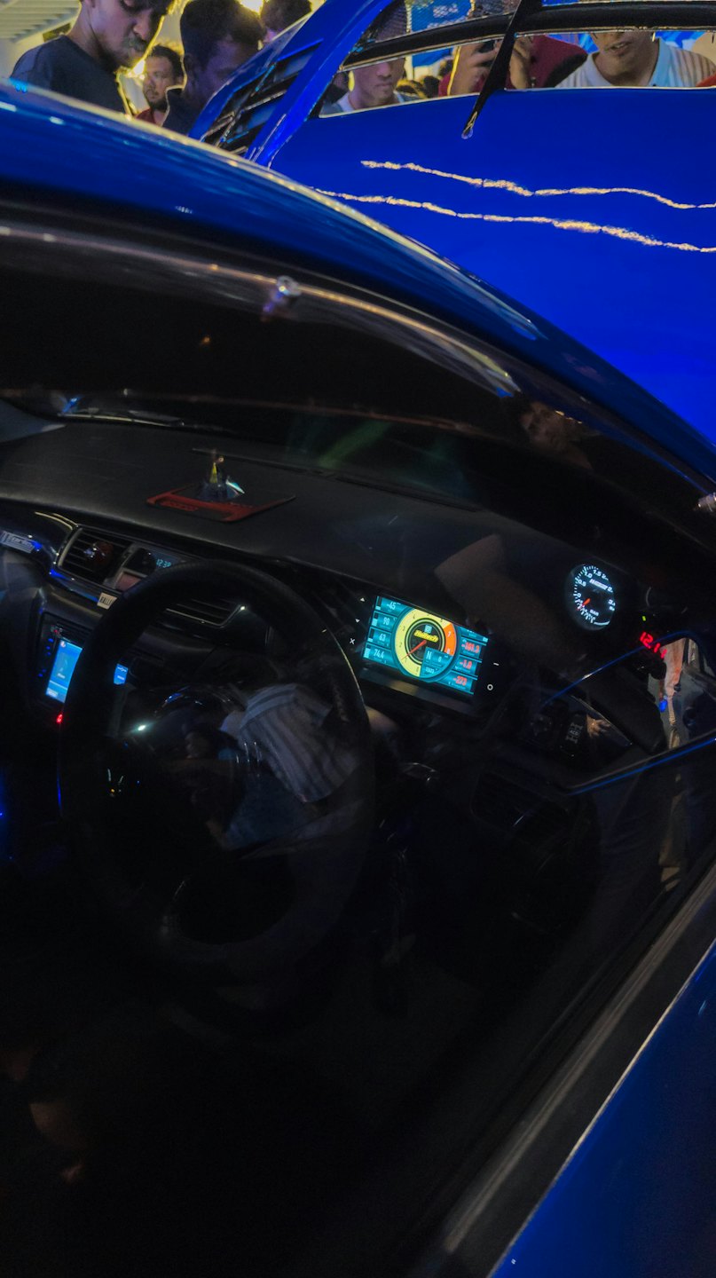 Mechanics inspect the engine of a blue car with glowing gauges.