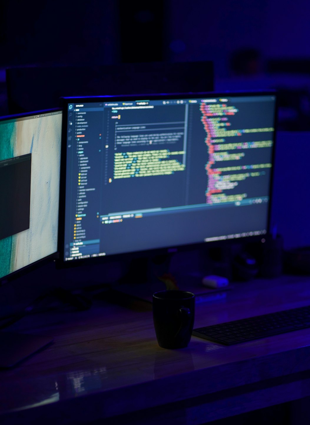 Two computer monitors displaying coding work on a wooden desk.